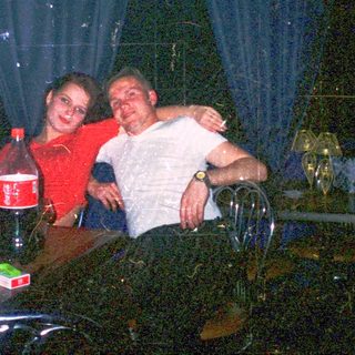 Two people hugging indoors at a dimly lit table with drinks.