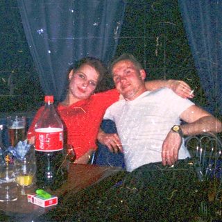 Two people hugging indoors at a dimly lit table with drinks.