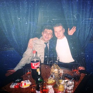 Two men posing indoors with drinks, party atmosphere.
