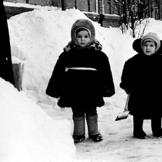 Two children shoveling snow in winter street.