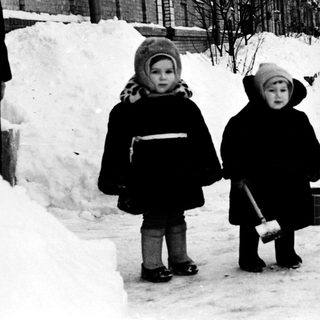Two children walking in snowy urban street.