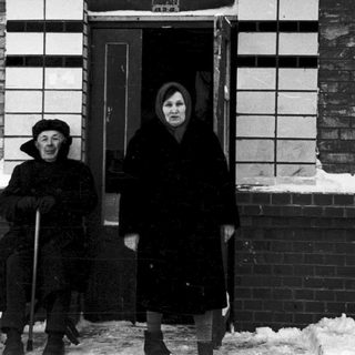 Two elderly individuals standing outside in winter snow.