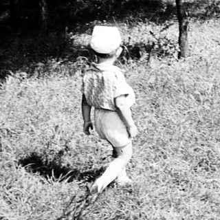 Child walking barefoot in grassy outdoor area.