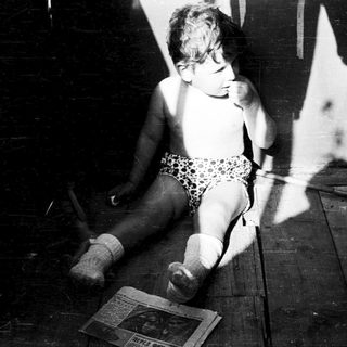 Toddler sitting on floor in dim light.
