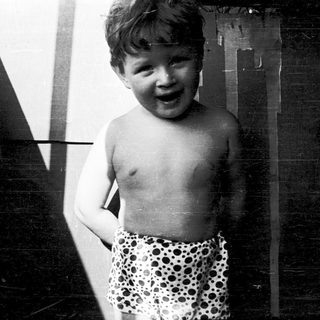 Shirtless boy smiling in polka-dot swim shorts.