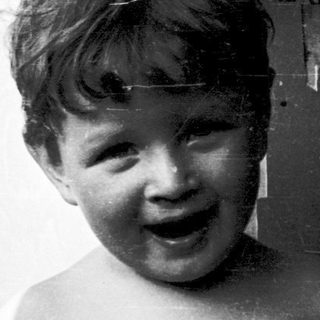 Shirtless boy smiling in polka-dot swim shorts.