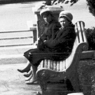 Two people sitting on bench in park near tall column.