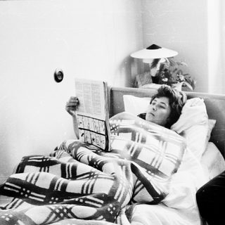 Man reading newspaper to sick woman in bed.