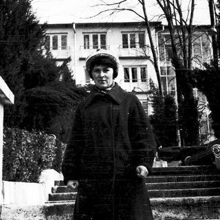 Woman in winter coat posing outdoors near grand building.