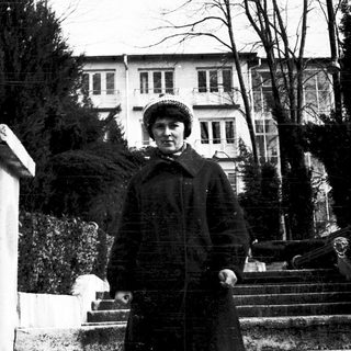 Woman in winter coat posing outdoors near grand building.