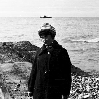 Person standing by icy coastal breakwater near ocean.