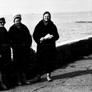 Three women standing by the seaside in winter attire.