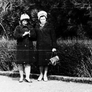 Two young girls in vintage clothing pose outdoors.