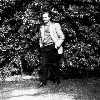 Man in suit standing confidently outdoors near trees.