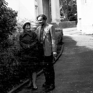 Two people posing outdoors in vintage attire.