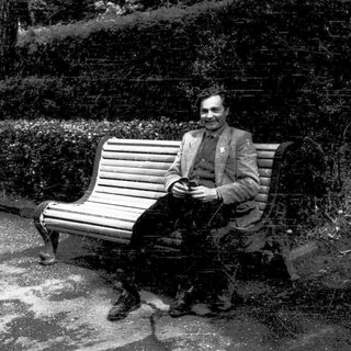Man sitting on bench reading newspaper outdoors.