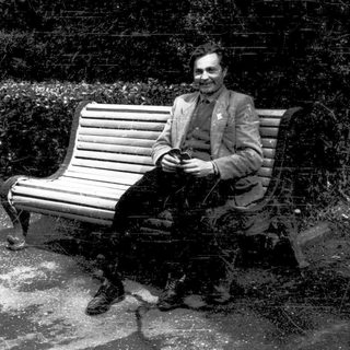 Man sitting on bench reading newspaper outdoors.