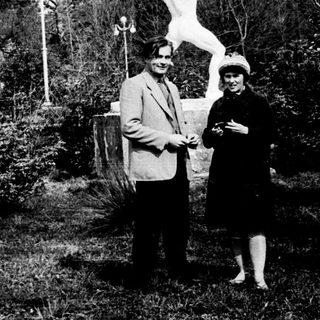 Two people posing with a statue in a garden.
