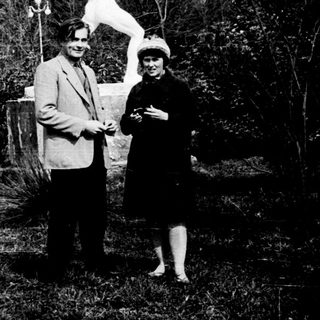 Two people posing with a statue in a garden.