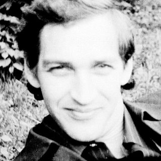 A man smiling outdoors in a grassy area.