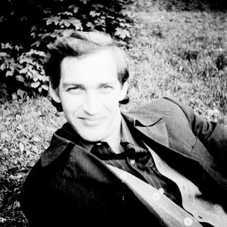 A man smiling outdoors in a grassy area.