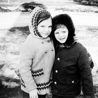 Two children smiling together in winter clothing.