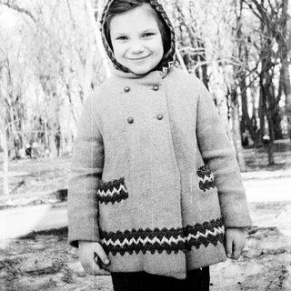 Young girl wearing winter coat and headscarf outdoors.