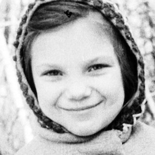 Young girl wearing winter coat and headscarf outdoors.