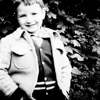 Young boy smiling outdoors in vintage clothing.