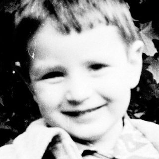 Young boy smiling outdoors in vintage clothing.