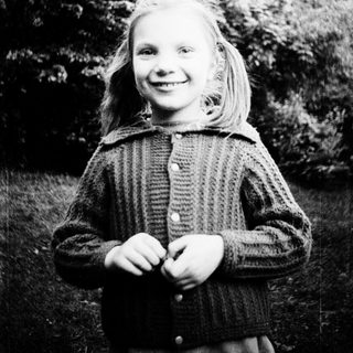 Young girl smiling outdoors in vintage sweater.