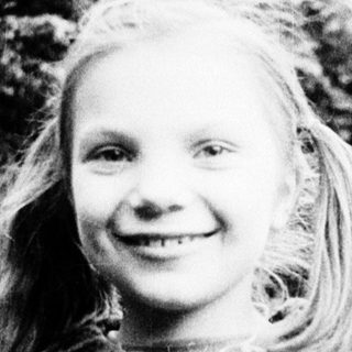 Young girl smiling outdoors in vintage sweater.