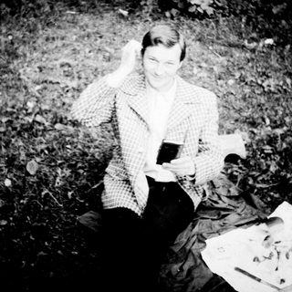 Person sitting outdoors enjoying drink and sketchbook.