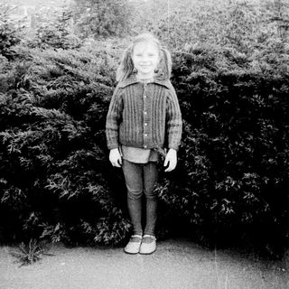 Young girl standing outdoors near dense greenery.