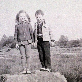 Two children standing together on a rock.