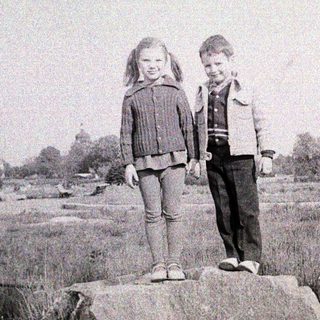 Two children standing together on a rock.