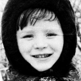 Child smiling outdoors in winter attire.