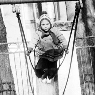 Child swinging on ropes in damaged urban area.