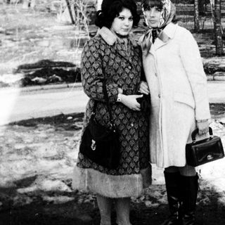 Two women posing closely outdoors in winter attire.