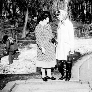 Two women conversing outdoors in winter attire.