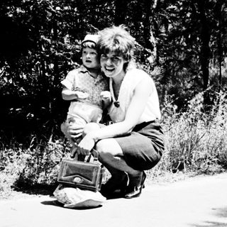 A woman kneeling outdoors holding a child.