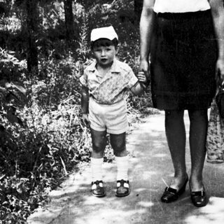 A woman and child walking hand-in-hand on a shaded path.