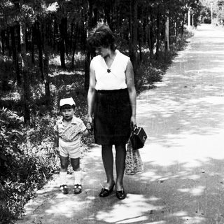 A woman and child walking hand-in-hand on a shaded path.
