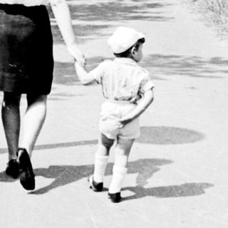 A woman and child walking hand-in-hand on a rural path.