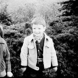 Two children smiling outdoors in vintage clothing.