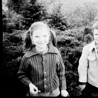 Two children smiling outdoors in vintage clothing.