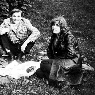 Three people sitting outdoors, posing together near a picnic blanket.