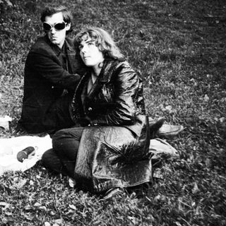 Three people sitting outdoors on blanket.
