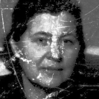 A woman sitting indoors, looking thoughtful, in aged surroundings.