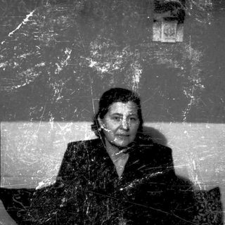 A woman sitting indoors, looking thoughtful, in aged surroundings.